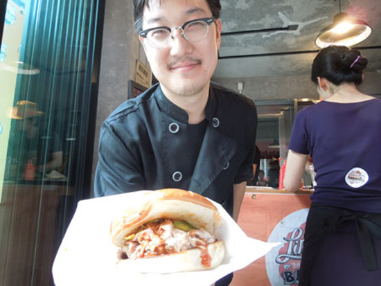 Linus Kim of “Linus’ Bama Style Barbeque” shows off a pulled pork sandwich.