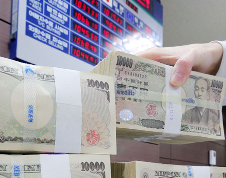 Bundles of 10,000-yen banknotes are stacked in front of an electronic billboard showing real-time currency exchange rates at a Korea Exchange Bank branch in Seoul. (Yonhap)