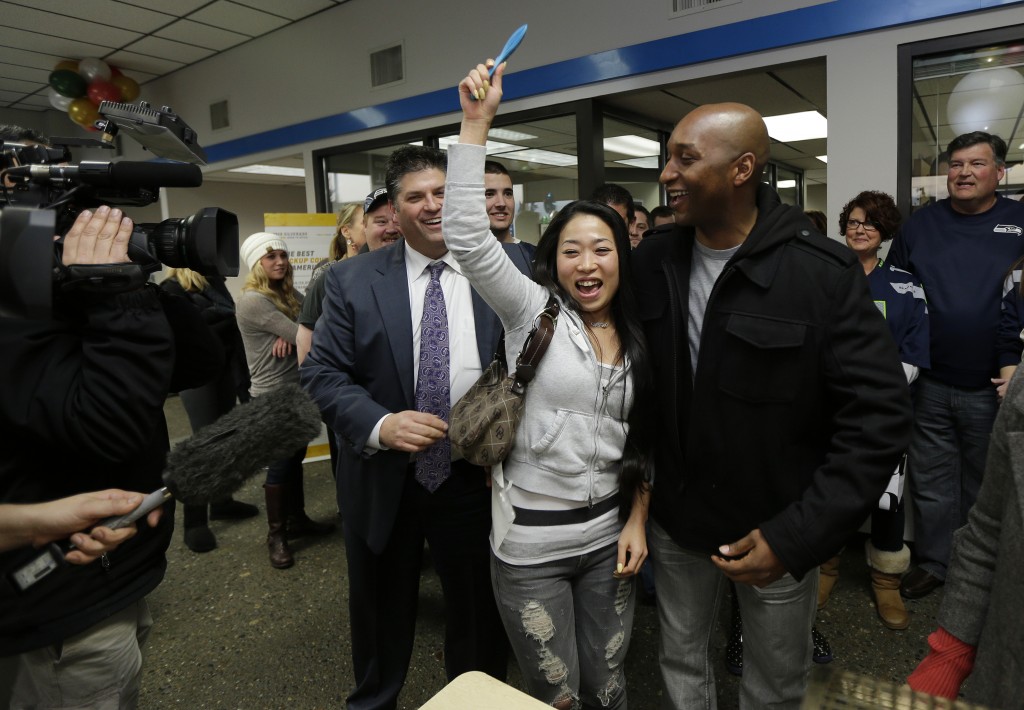 Yujin Oliver, the woman in the middle, and her husband Samonie Oliver, right, are celebrating next to Mike Gates, left, general manager of Jet Chevrolet in Federal Way, Wash., Monday, Dec. 16, 2013, after their ticket was drawn as one of 12 $35,000 winners in a dealership-sponsored raffle held only if the Seattle Seahawks shut out the New York Giants in last Sunday's NFL football game. The Seahawks defeated the Giants 23-0, and the winners drawn Monday will soon be receiving checks from the insurance policy purchased by the dealership to fund the drawing. (AP Photo/Ted S. Warren)  
