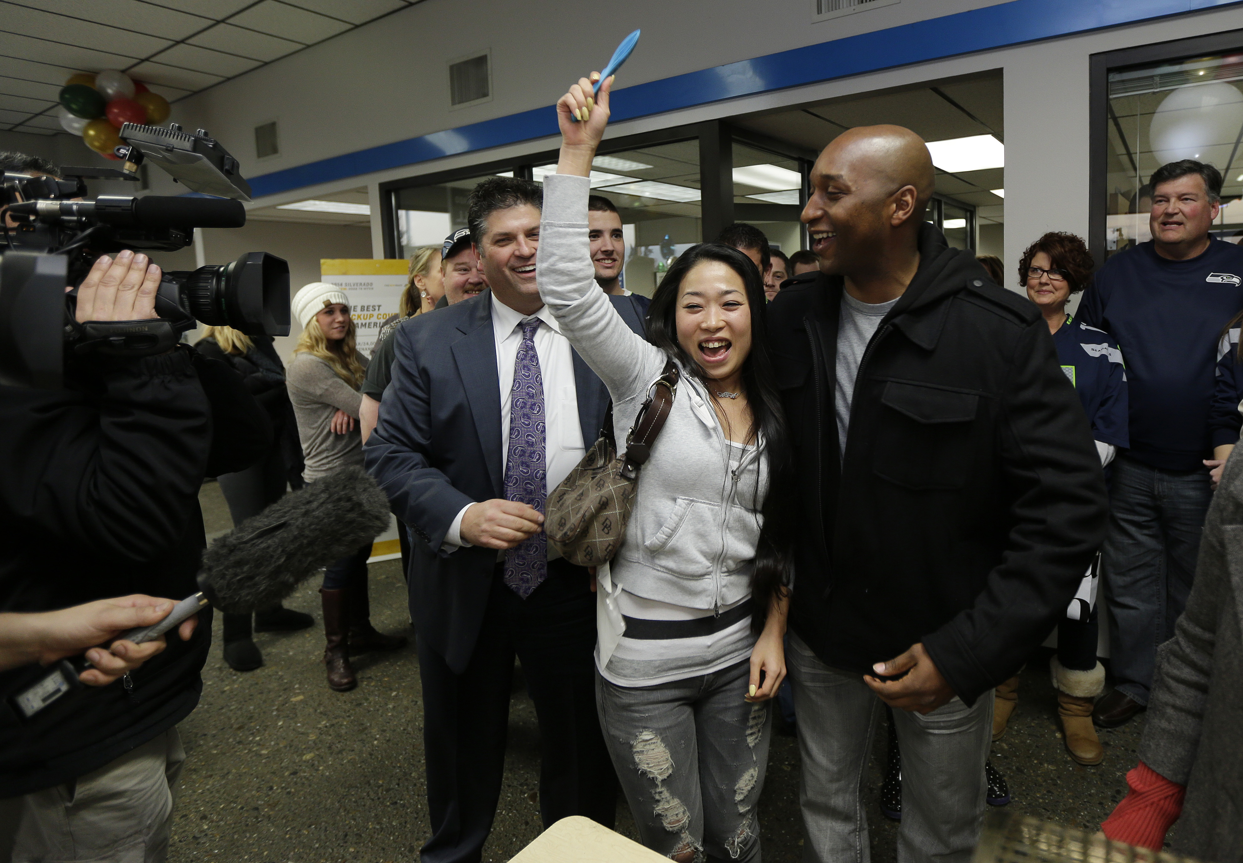 Yujin Oliver, the woman in the middle, and her husband Samonie Oliver, right, are celebrating next to Mike Gates, left, general manager of Jet Chevrolet in Federal Way, Wash., Monday, Dec. 16, 2013, after their ticket was drawn as one of 12 $35,000 winners in a dealership-sponsored raffle held only if the Seattle Seahawks shut out the New York Giants in last Sunday's NFL football game. The Seahawks defeated the Giants 23-0, and the winners drawn Monday will soon be receiving checks from the insurance policy purchased by the dealership to fund the drawing. (AP Photo/Ted S. Warren)