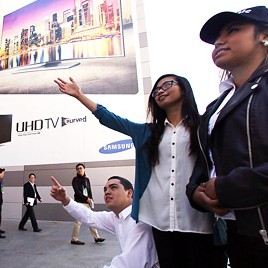 Visitors look at a banner promoting the world’s first curved ultra high-definition (UHD) TV manufactured by Samsung Electronics at the Las Vegas Convention Center, Monday (KST). (Courtesy of Samsung Electronics)