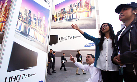 Visitors look at a banner promoting the world’s first curved ultra high-definition (UHD) TV manufactured by Samsung Electronics at the Las Vegas Convention Center, Monday (KST). (Courtesy of Samsung Electronics)