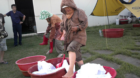 Women soak a pile of cloth in persimmon extract by stepping on it. The process is used to color the cloth evenly.
