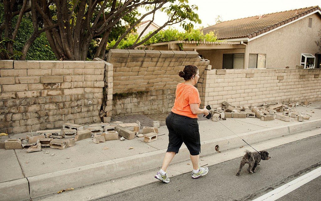 A woman walks her dog past a broken block wall in Fullerton, Calif., on Saturday, March 29, 2014, after an earthquake hit Orange County Friday night. More than 100 aftershocks have rattled Orange County south of Los Angeles where a magnitude-5.1 earthquake struck Friday. Despite the relatively minor damage, no injuries have been reported. (AP Photo/The Orange County Register, Ken Steinhardt)