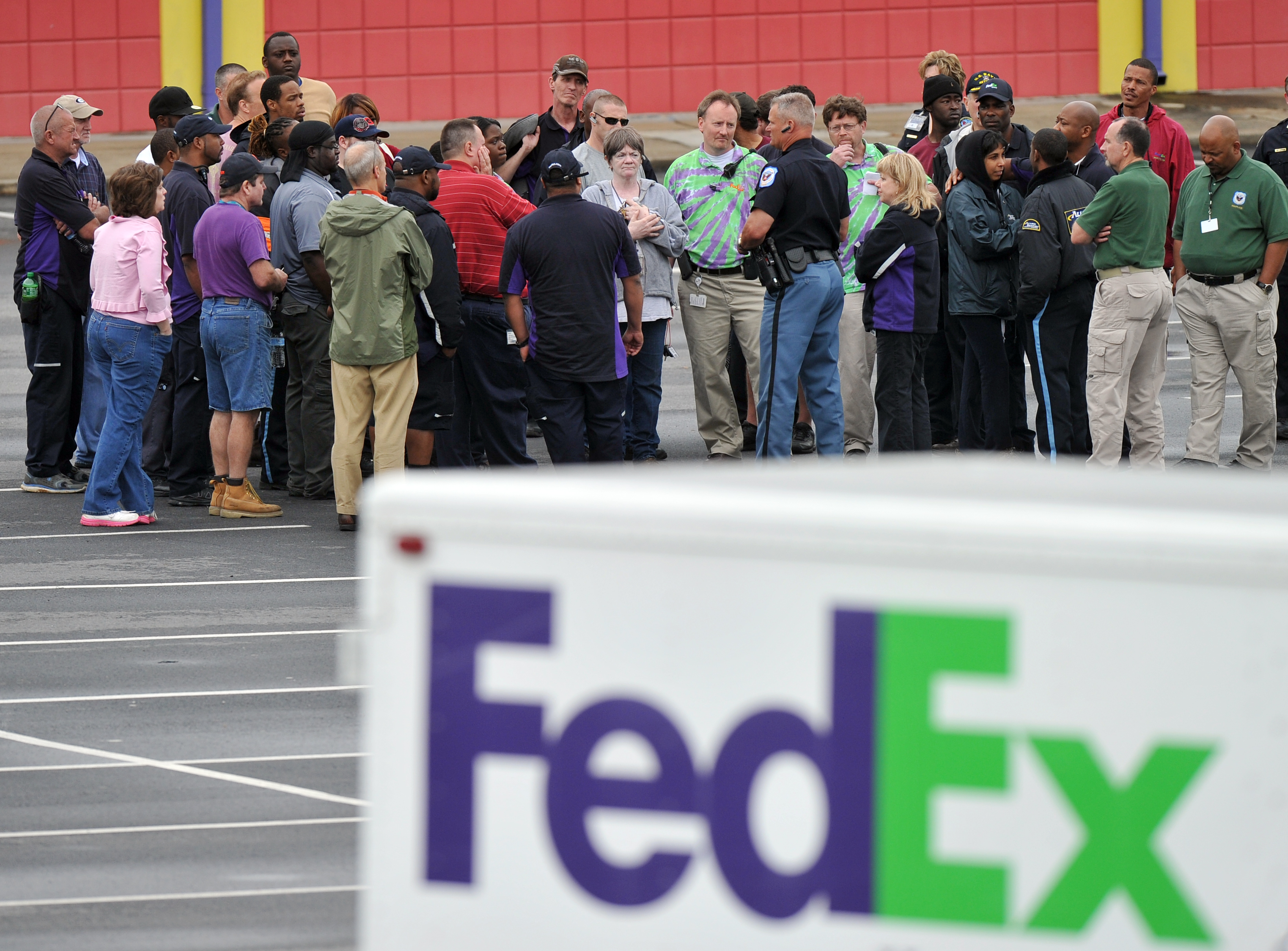 A Cobb County Police Officer speaks to FedEx employees and family members gathered at the parking lot of a skating rink located near the shipping facility where a gunman open fire in Kennesaw, Ga., on Tuesday, April 29, 2014. A shooter described as being armed with an assault rifle and having bullets strapped across his chest "like Rambo" opened fire Tuesday morning at a FedEx station outside Atlanta, wounding at least six people before police found the suspect dead from an apparent self-inflicted gunshot. (AP Photo/Atlanta Journal-Constitution, Brant Sanderlin)