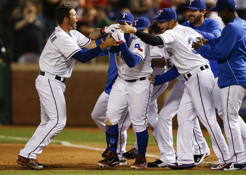 Texas Rangers' Shin-Soo Choo, center, is swarmed by teammates including J.P. Arencibia, left, and Martin Perez, right, after drawing a bases-loaded game-winning walk in a baseball game against the Philadelphia Phillies, Wednesday, April 2, 2014, in Arlington, Texas. The Rangers won 4-3. (AP Photo/Jim Cowsert)