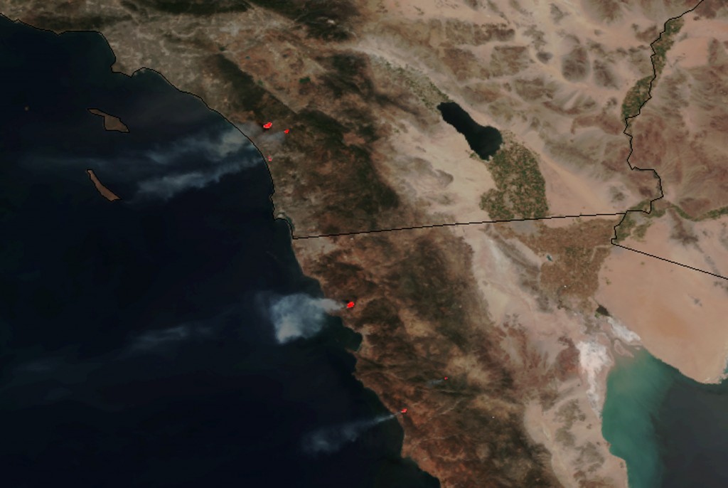 This May 14, 2014 image provided by NASA shows numerous large wildfires burning across sections of northern Baja and southern California, producing plumes of moderate to dense smoke and combining with blowing dust and sand moving west off the coast and well into the Pacific Ocean. Nine fires in all were burning an area of more than 14 square miles amid a heat wave and dry conditions, said San Diego County officials, who warned also of poor air quality with black and gray smoke wafting over the region. (AP Photo/NASA)