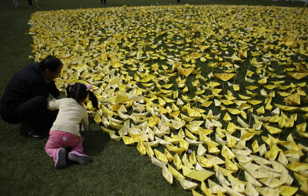 A girl with a man put a paper ship for the victims and missing passengers of the sunken ferry Sewol at a group memorial altar in Seoul, South Korea, Wednesday, May 7, 2014. (AP Photo/Lee Jin-man)