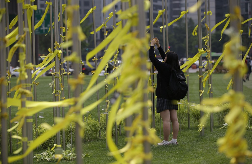 A girl ties yellow ribbons with messages for missing passengers aboard the sunken ferry boat Sewol in the water off the southern coast, in Seoul, South Korea, Friday, May 2, 2014. More than 300 people are dead or missing in the disaster that has caused widespread grief, anger and shame. (AP Photo/Lee Jin-man)