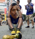 A Japanese soccer fan wearing a mask of Japanese soccer player Yuto Nagatomo sits on a street after the group C World Cup soccer match between Japan and Colombia outside a public viewing venue in Tokyo early Wednesday, June 25, 2014. For Japan, this World Cup has been a nightmare revisited: The Asian champions seize momentum with waves of dangerous attack, and little payoff. Then their opponent's talismanic player comes on as a second-half substitute - and Japan wilts under pressure. (AP Photo/Kyodo News)