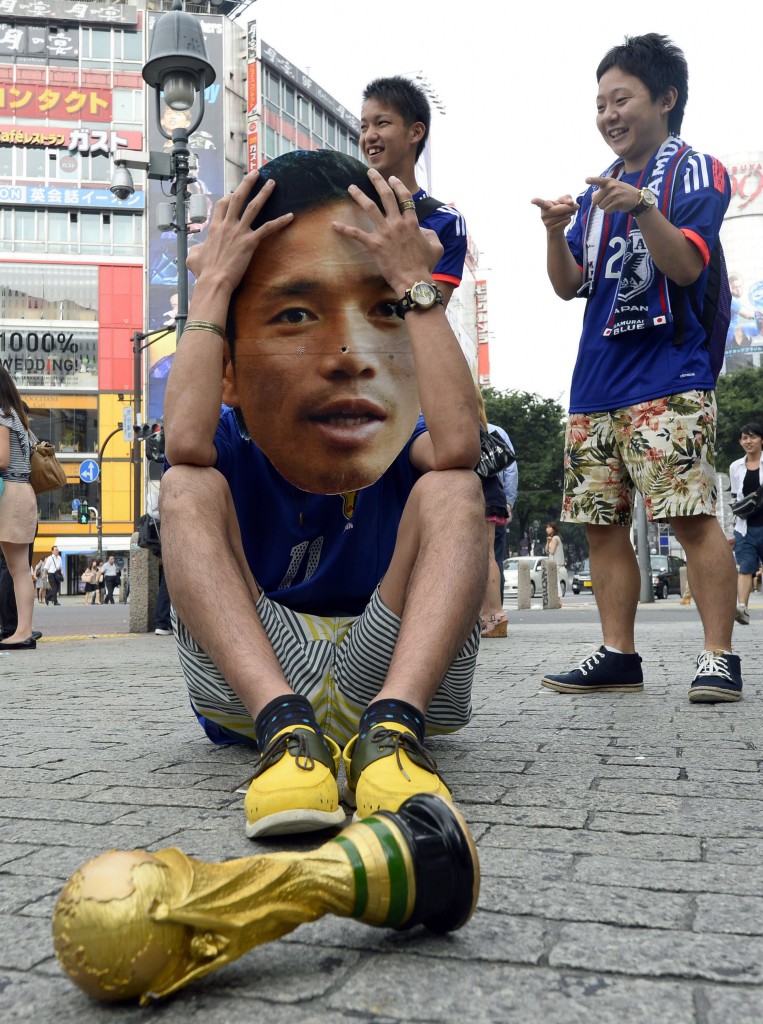 A Japanese soccer fan wearing a mask of Japanese soccer player Yuto Nagatomo sits on a street after the group C World Cup soccer match between Japan and Colombia outside a public viewing venue in Tokyo early Wednesday, June 25, 2014. For Japan, this World Cup has been a nightmare revisited: The Asian champions seize momentum with waves of dangerous attack, and little payoff. Then their opponent's talismanic player comes on as a second-half substitute - and Japan wilts under pressure. (AP Photo/Kyodo News) 