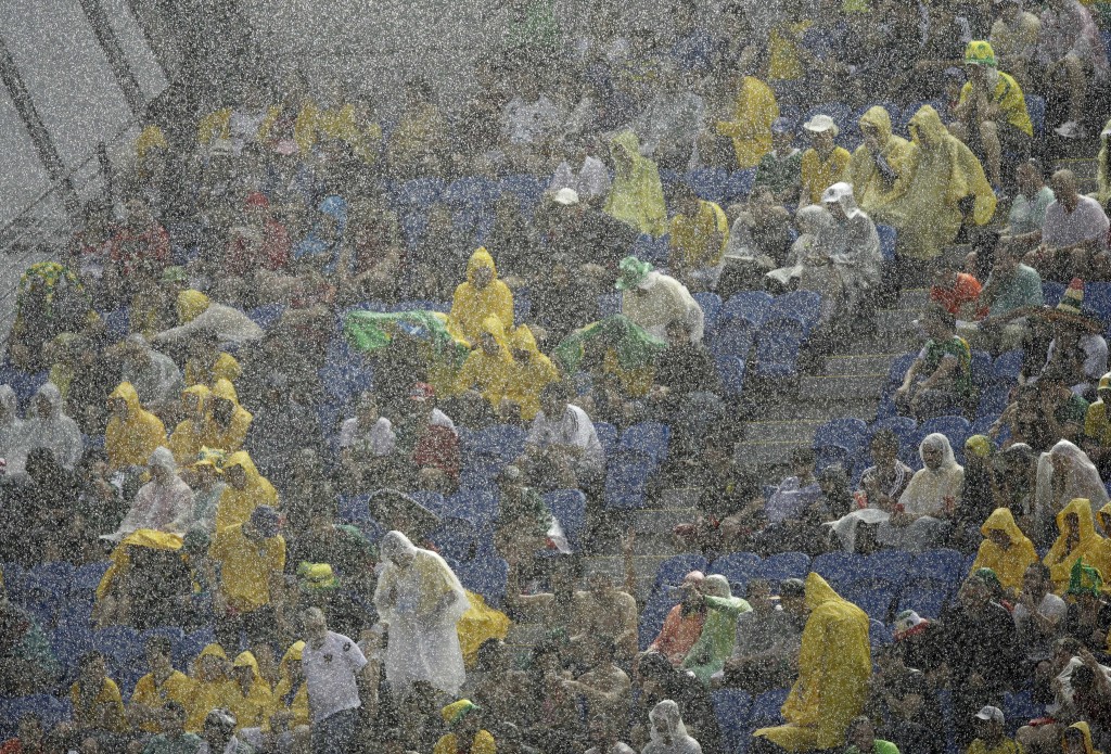 Spectators sit under pouring rain as they watch the group A World Cup soccer match between Mexico and Cameroon in the Arena das Dunas in Natal, Brazil, Friday, June 13, 2014. (AP Photo/Hassan Ammar)