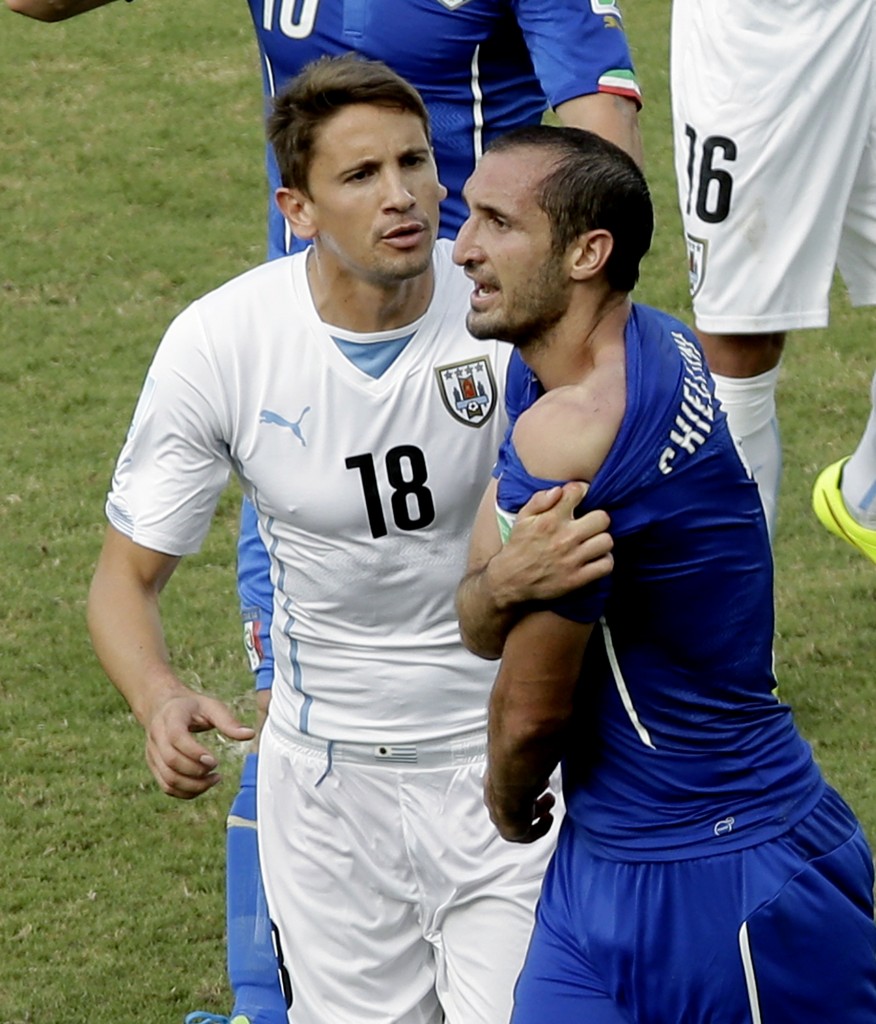 Italy's Giorgio Chiellini, right, shows his shoulder after colliding with Uruguay's Luis Suarez's mouth as Uruguay's Gaston Ramirez (18) watches during the group D World Cup soccer match between Italy and Uruguay at the Arena das Dunas in Natal, Brazil, Tuesday, June 24, 2014. (AP Photo/Hassan Ammar)