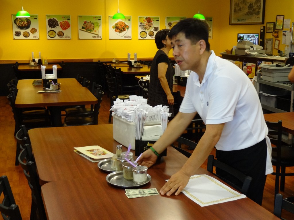 A waiter picks up a tip left at a table in a Koreatown restaurant.