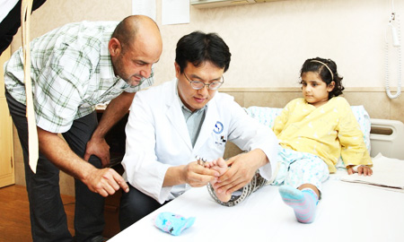 Amer Alwan Ibreesam, left, looks on as professor Cho Jae-ho of Ajou University Hospital examines the leg of his daughter Tiba at the hospital in Suwon, Gyeonggi Province. Hanwha Engineering and Construction brought Tiba from Iraq to get surgery on her leg in Korea. (Courtesy of Hanwha Engineering and Construction)