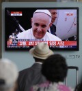 People watch a live TV news program showing Pope Francis' arrival at the Seoul Railway Station in Seoul, South Korea, Thursday, Aug. 14, 2014. Pope Francis arrived Thursday in South Korea on the first papal visit to the Asian nation in a quarter century, stepping off the plane onto a red carpet and greeting President Park Geun-hye. (AP Photo/Lee Jin-man)