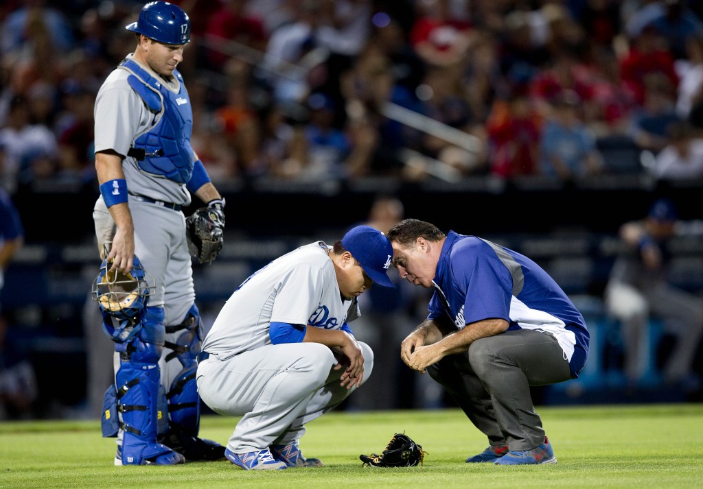 A member of the Los Angeles Dodgers training staff talks to injured starting pitcher Hyun-Jin Ryu (99) as catcher A.J. Ellis looks on at left, in the sixth inning of a baseball game against the Atlanta Braves Wednesday, Aug. 13, 2014, in Atlanta. Ryu left the game under his own power. (AP Photo/John Bazemore)