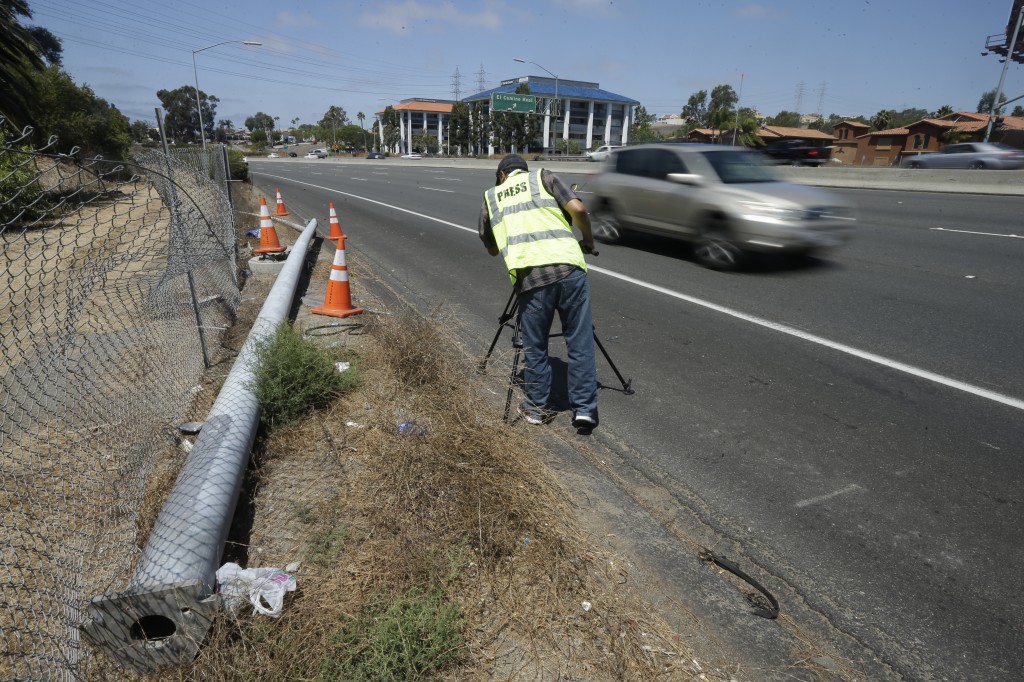 A cameraman films a broken power pole along the highway after a fatal crash Friday, Aug. 22, 2014, in Oceanside, Calif. Three Japanese college students were killed and five other foreign students were injured when a car carrying them veered off a California freeway and struck a power pole, officials said Friday. (AP Photo/Gregory Bull)