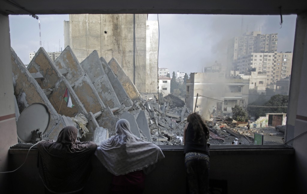 A Palestinian family looks from a window to the rubble of the collapsed 15-story Basha Tower following early morning Israeli airstrikes in Gaza City, Tuesday, Aug. 26, 2014. Israel bombed two Gaza City high-rises with dozens of homes and shops Tuesday, collapsing the 15-story Basha Tower and severely damaging the Italian Complex in a further escalation in seven weeks of cross-border fighting with Hamas. (AP Photo/Khalil Hamra)