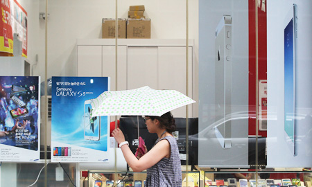 A woman walks by advertisement posters of Samsung Electronics' Galaxy S5, Apple's iPhone 5s and iPad Air at a mobile phone shop in Seoul, Wednesday. (AP-Yonhap)
