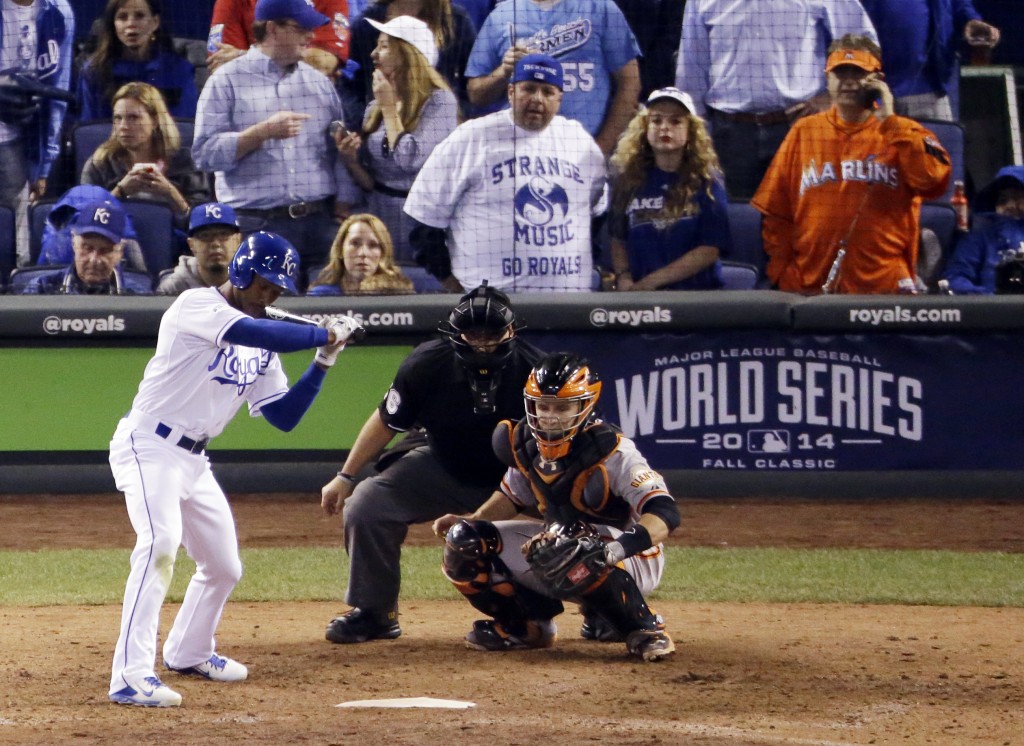 In this Wednesday, Oct. 22, 2014, photo, Miami Marlins fan Laurence Leavy, rear right, is shown wearing a bright orange Marlins jersey during Game 2 of baseball's World Series in Kansas City, Mo. Leavy's orange Marlins jersey made him easy to spot amid a sea of Kansas City Royals blue. He said a Royals official approached him offering to move him to the team owner's suite, but Leavy declined. (AP Photo/Charlie Riedel)