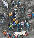 Rescuers struggle in the ash-covered muddy slope as they carry down the body of a newly-found victim from the summit of Mount Ontake in central Japan, Saturday, Oct. 4, 2014. Rescuers on Saturday retrieved four more bodies near the summit of the Japanese volcano that erupted last weekend, raising the death toll to 51, authorities said. (AP Photo/Kyodo News)
