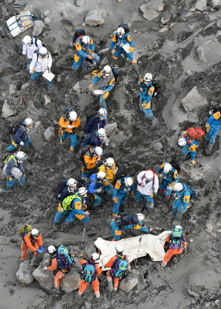Rescuers struggle in the ash-covered muddy slope as they carry down the body of a newly-found victim from the summit of Mount Ontake in central Japan, Saturday, Oct. 4, 2014. Rescuers on Saturday retrieved four more bodies near the summit of the Japanese volcano that erupted last weekend, raising the death toll to 51, authorities said. (AP Photo/Kyodo News) 