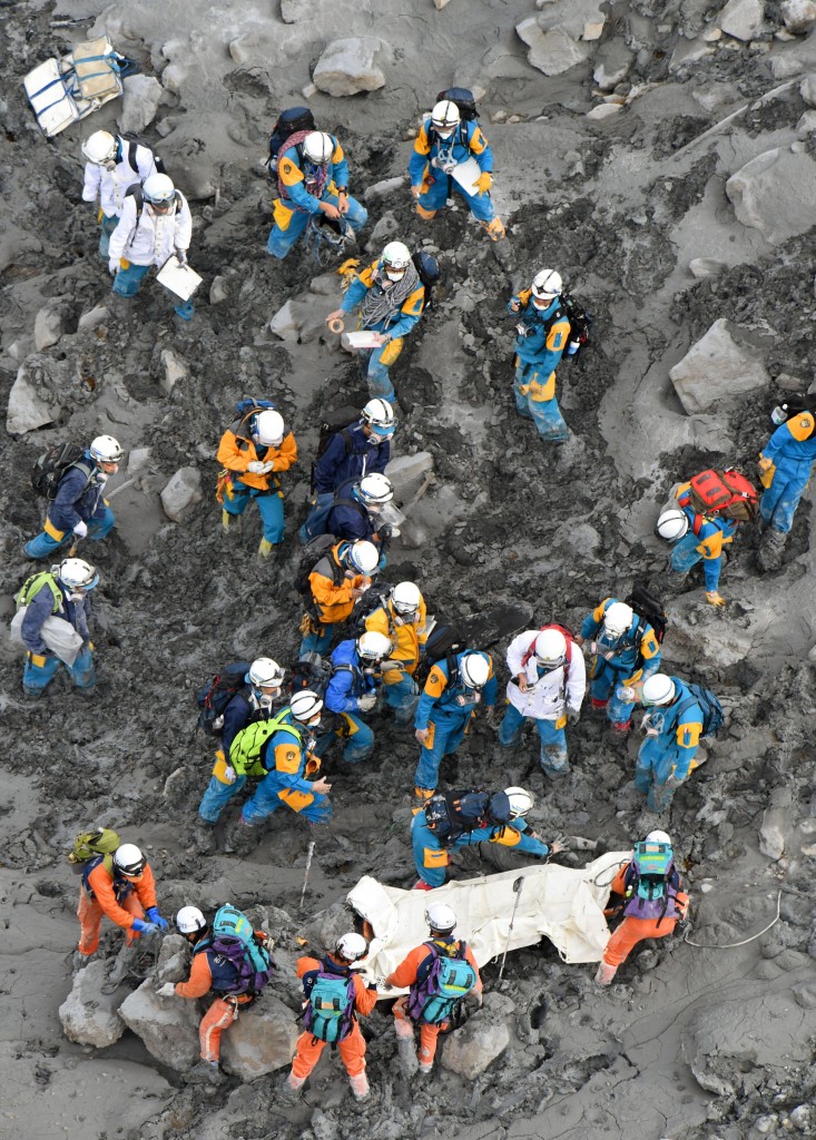 Rescuers struggle in the ash-covered muddy slope as they carry down the body of a newly-found victim from the summit of Mount Ontake in central Japan, Saturday, Oct. 4, 2014. Rescuers on Saturday retrieved four more bodies near the summit of the Japanese volcano that erupted last weekend, raising the death toll to 51, authorities said. (AP Photo/Kyodo News)