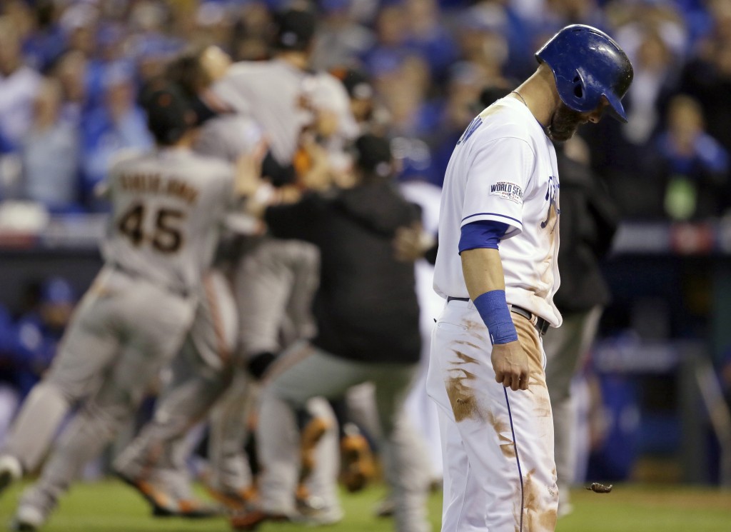 Kansas City Royals' Alex Gordon (4) walks off the field as San Francisco Giants players celebrates after Game 7 of baseball's World Series Wednesday, Oct. 29, 2014, in Kansas City, Mo. The Giants won 3-2 to win the series. (AP Photo/Charlie Neibergall)