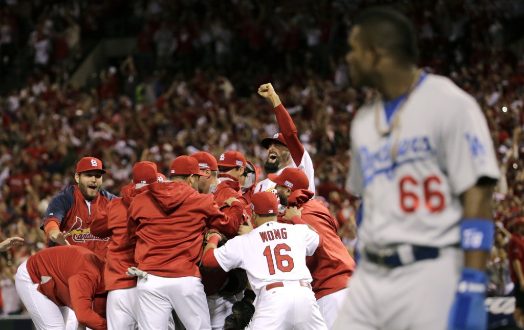 St. Louis Cardinals players celebrate after their 3-2 win over Los Angeles Dodgers in Game 4 of baseball's NL Division Series Tuesday, Oct. 7, 2014, in St. Louis as Los Angeles Dodgers right fielder Yasiel Puig, right, looks on. (AP Photo/Charles Rex Arbogast)