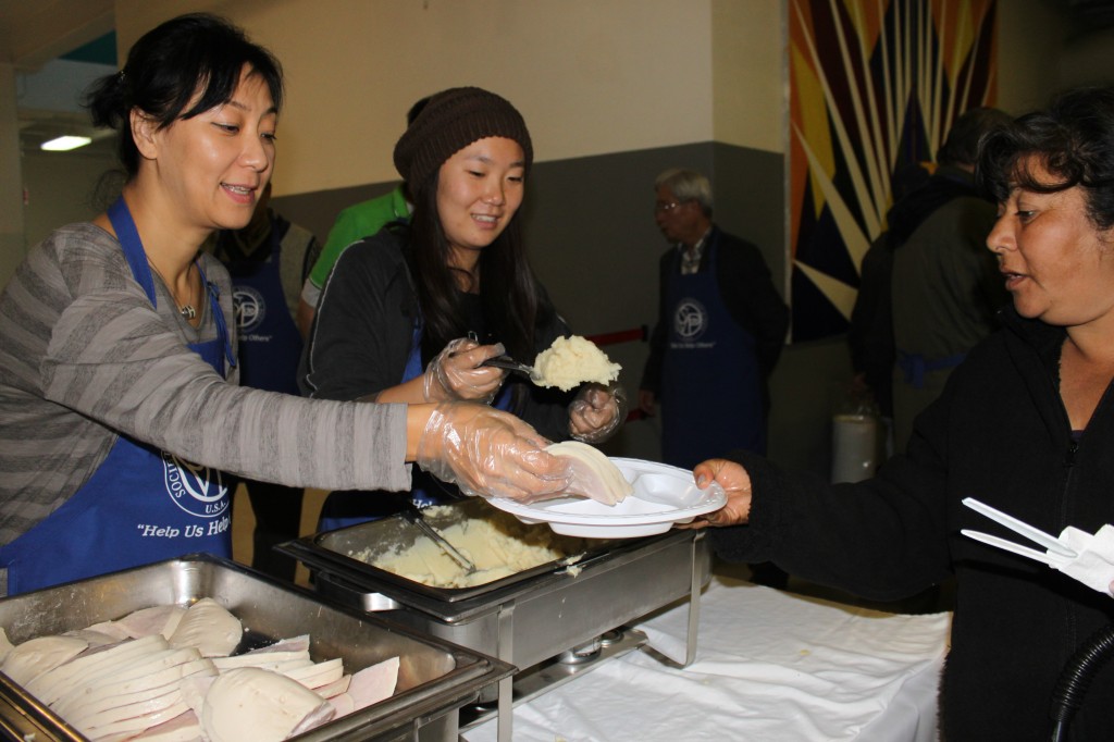 Korean women serve turkey and mashed potatoes to a homeless woman.