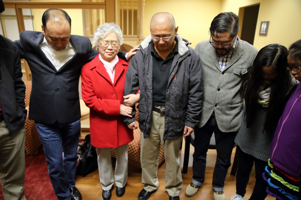 This photo provided by Derek Sciba shows Kenneth Bae, center, and his mother Myunghee Bae, in red coat, praying with other family members after his release from North Korea, Saturday Nov. 8, 2014.  (AP Photo/Derek Sciba)