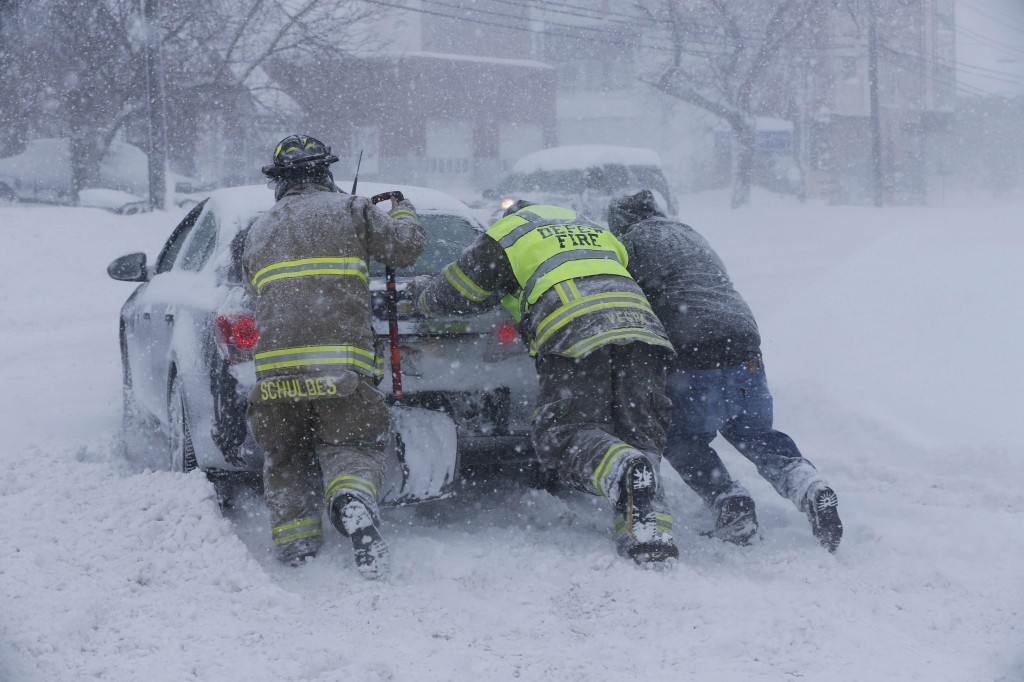 Firefighters from West End Hose Company in Depew, N.Y. help a stuck motorist on Transit Road, Tuesday, Nov. 18, 2014.  Several feet of lake-effect snow paralyzed the Buffalo area Tuesday, forcing state troopers to deliver blankets and other supplies to motorists stranded on the New York State Thruway and adding an ominous note to a wintry season thats already snarling travel and numbing fingers from the Midwest to the Carolinas.  (AP Photo/The Buffalo News, Derek Gee)