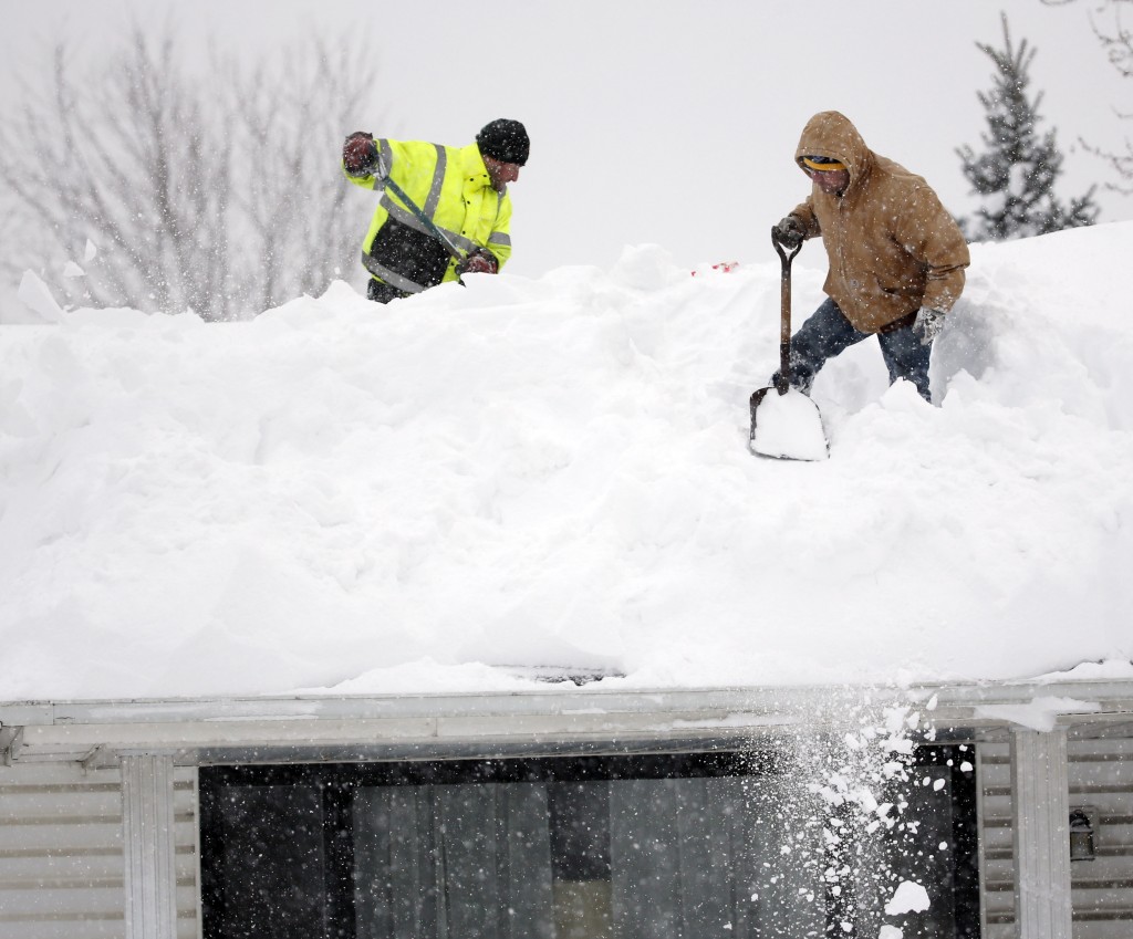 Mark Settlemyer, left, gets help clearing snow from the roof of his mother's house from Ken Wesley on Wednesday, Nov. 19, 2014, in Lancaster, N.Y. Lake-effect snow pummeled areas around Buffalo for a second straight day, leaving residents stuck in their homes as officials tried to clear massive snow mounds with another storm looming. (AP Photo/Mike Groll)