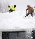 Mark Settlemyer, left, gets help clearing snow from the roof of his mother's house from Ken Wesley on Wednesday, Nov. 19, 2014, in Lancaster, N.Y. Lake-effect snow pummeled areas around Buffalo for a second straight day, leaving residents stuck in their homes as officials tried to clear massive snow mounds with another storm looming. (AP Photo/Mike Groll)