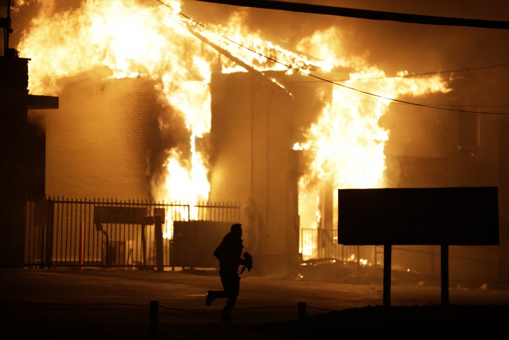 A man runs away from the burning storage facility after  the announcement of the grand jury decision Monday, Nov. 24, 2014, in Ferguson, Mo. A grand jury has decided not to indict Ferguson police officer Darren Wilson in the death of Michael Brown, the unarmed, black 18-year-old whose fatal shooting sparked sometimes violent protests. (AP Photo/David Goldman)