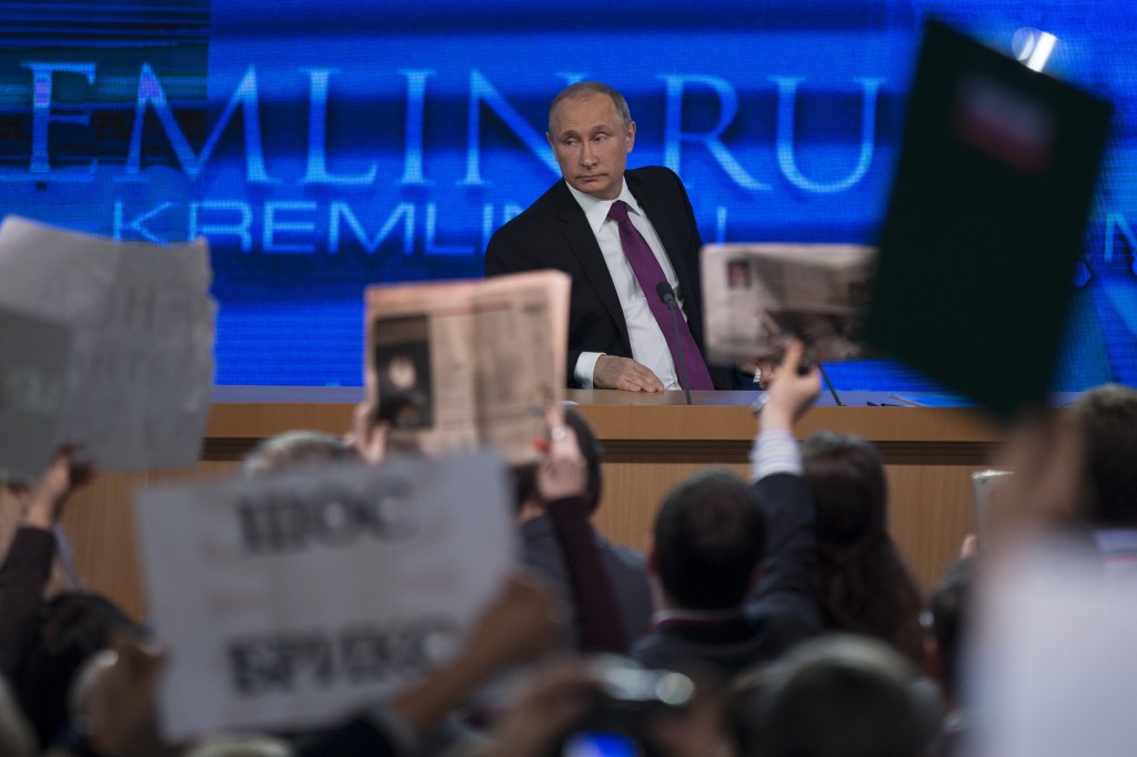 Journalists raise hands and posters and papers to attract attention, as Russian President Vladimir Putin, background, listens to a question, during his annual news conference in Moscow, Russia, Thursday, Dec. 18, 2014. The Russian economy will rebound and the ruble will stabilize, Russian President Vladimir Putin said Thursday at his annual press conference, he also said Ukraine must remain one political entity, voicing hope that the crisis could be solved through peace talks. (AP Photo/Pavel Golovkin)