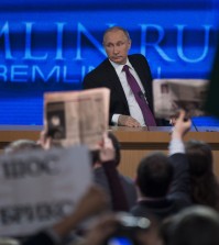 Journalists raise hands and posters and papers to attract attention, as Russian President Vladimir Putin, background, listens to a question, during his annual news conference in Moscow, Russia, Thursday, Dec. 18, 2014. The Russian economy will rebound and the ruble will stabilize, Russian President Vladimir Putin said Thursday at his annual press conference, he also said Ukraine must remain one political entity, voicing hope that the crisis could be solved through peace talks. (AP Photo/Pavel Golovkin)