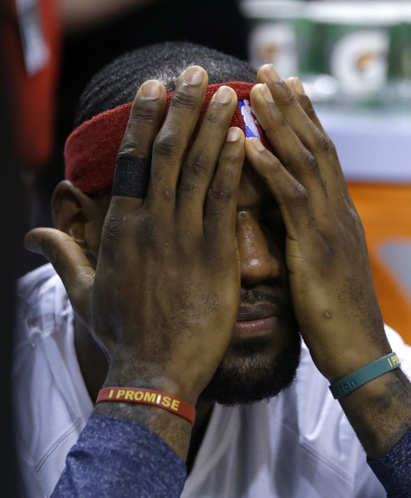 Cleveland Cavaliers forward LeBron James covers his face while sitting on the bench before an NBA basketball game against the Miami Heat, Thursday, Dec. 25, 2014, in Miami. (AP Photo/Lynne Sladky)