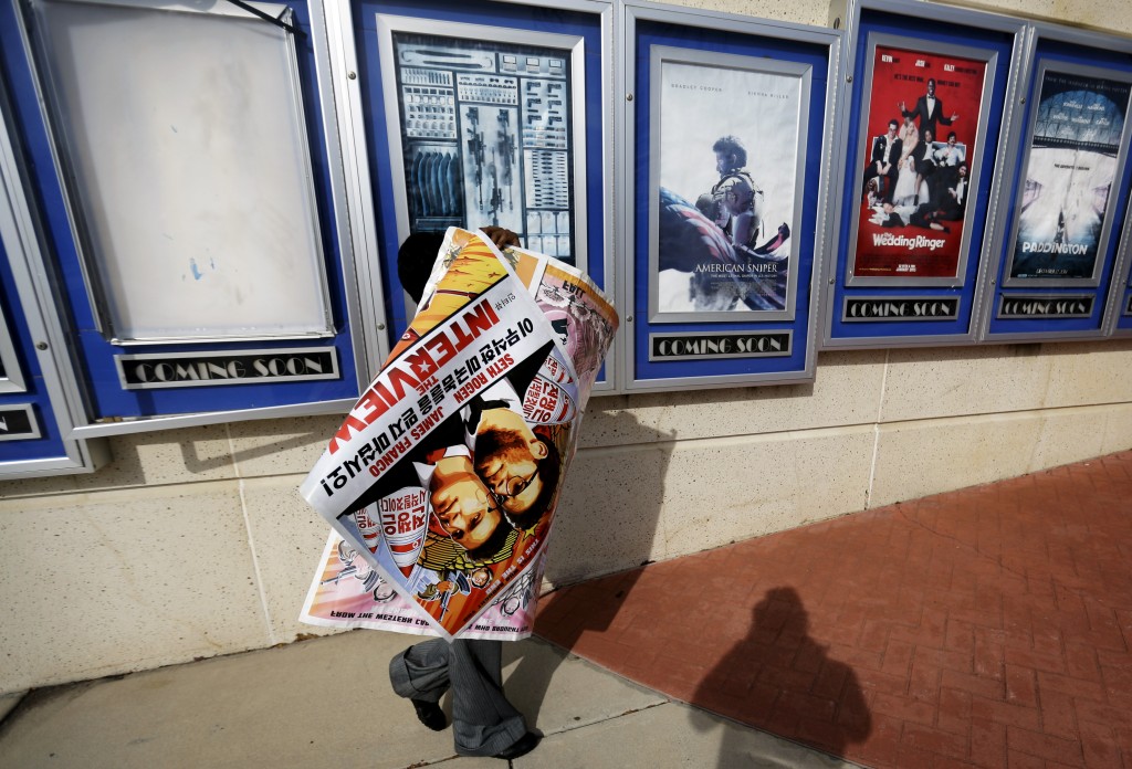 A poster for the movie "The Interview" is carried away by a worker after being pulled from a display case at a Carmike Cinemas movie theater, Wednesday, Dec. 17, 2014, in Atlanta. Georgia-based Carmike Cinemas has decided to cancel its planned showings of "The Interview" in the wake of threats against theatergoers by the Sony hackers. (AP Photo/David Goldman)