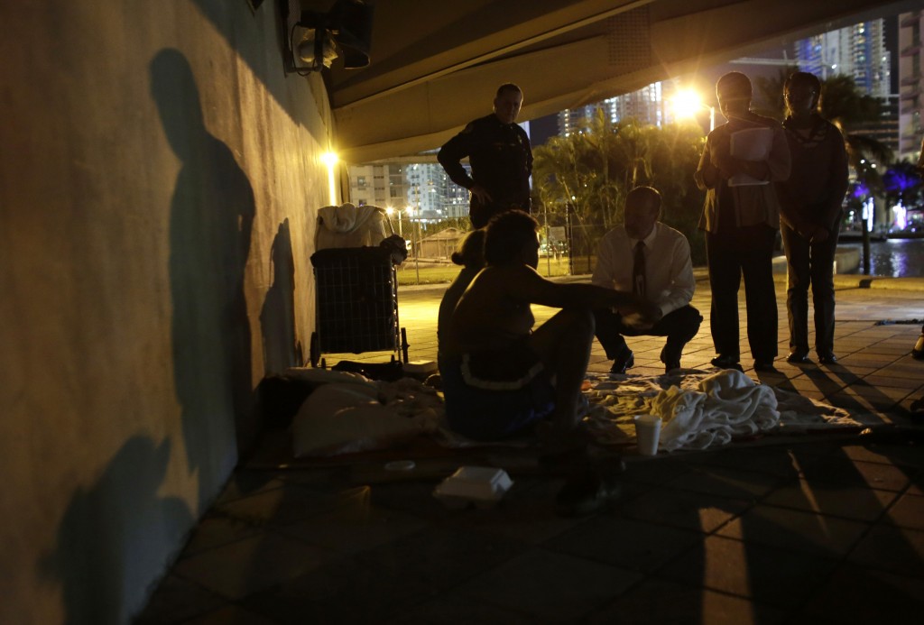 Ron Book, chairman of the Miami-Dade County Homeless Trust, center, kneeling, talks with a homeless couple sleeping under a bridge during the Point In Time Homeless Census, Thursday, Jan. 22, 2015, in Miami. The couple agreed to be sent to a shelter for the night. As part of a federal push, Miami-Dade County is aiming to end veteran homelessness by 2015, and chronic homelessness by 2016. (AP Photo/Lynne Sladky)