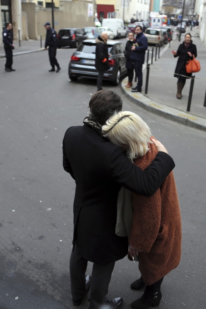 People stand outside the French satirical newspaper Charlie Hebdo's office after a shooting, in Paris, Wednesday, Jan. 7, 2015. Masked gunmen stormed the offices of a French satirical newspaper Wednesday, killing at least 12 people before escaping, police and a witness said. The weekly has previously drawn condemnation from Muslims. (AP Photo/Remy De La Mauviniere)