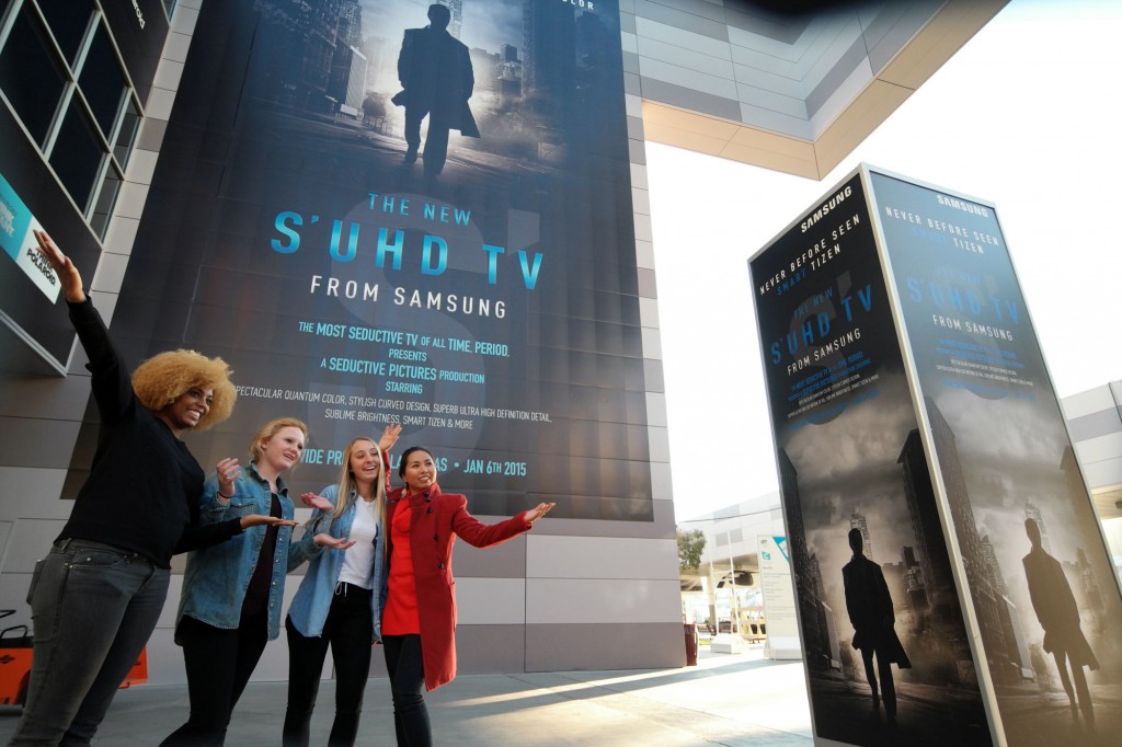 Visitors pose in front of Samsung's advertisement for its latest TV technology at the Consumer Electronics Summit in Las Vegas. (Korea Times file)