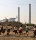 In this Tuesday, Feb. 24, 2015 photo, children play in front of chimneys standing at an under- construction coal-fired power plant, partially financed by the Japan Bank for International Cooperation, in Kudgi, India. Despite mounting protests, Japan continues to finance the building of coal-fired power plants with money earmarked for fighting climate change, with two new projects underway in India and Bangladesh, The Associated Press has found. (AP Photo/Aijaz Rahi)