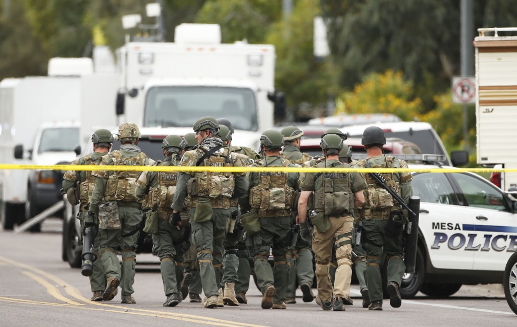 A SWAT team walks down the street near Adams Elementary School searching for a gunman on Wednesday, March 18, 2015 in Mesa, Ariz. A gunman wounded at least four people across multiple locations in the Phoenix suburb. The first shooting happened at a motel, and people were also wounded at a restaurant and nearby apartment complexes. (AP Photo/The Arizona Republic, Rob Schumacher)