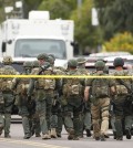 A SWAT team walks down the street near Adams Elementary School searching for a gunman on Wednesday, March 18, 2015 in Mesa, Ariz. A gunman wounded at least four people across multiple locations in the Phoenix suburb. The first shooting happened at a motel, and people were also wounded at a restaurant and nearby apartment complexes. (AP Photo/The Arizona Republic, Rob Schumacher)