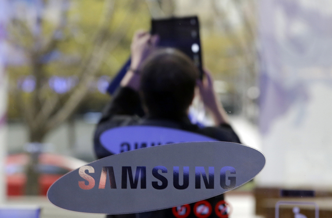 A visitor takes a picture near the logo of Samsung Electronics Co. outside its showroom in Seoul, South Korea, Tuesday, April 7, 2015. Samsung's quarterly operating earnings fell 31 percent from a year earlier but the drop wasn't as big as expected in a sign the smartphone and computer chip giant may be emerging from its profit slump. (AP Photo/Lee Jin-man)
