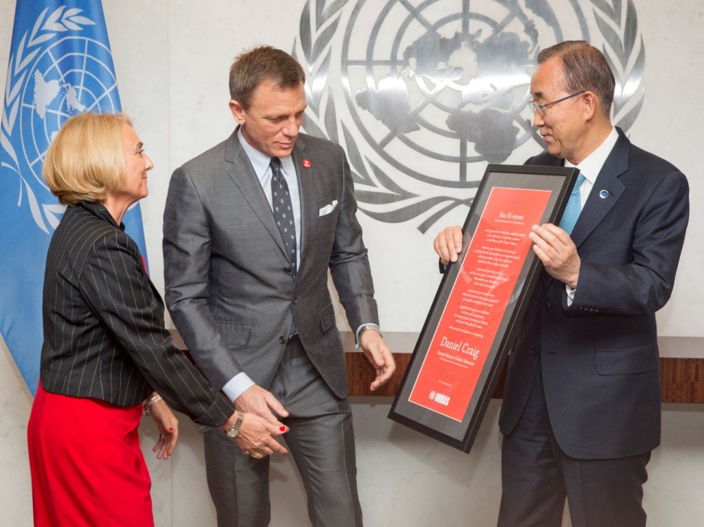 In this photo provided by the United Nations, U.N. Secretary General Ban Ki-moon, right, presents actor Daniel Craig, center, with a document designating him as the UN Global Advocate for the Elimination of Mines and Explosive Hazards, at United Nations headquarters, Tuesday, April 14, 2015. At left is Agnès Marcaillou, Director of the UN Mine Action Service. (Evan Schneider/The United Nations via AP)