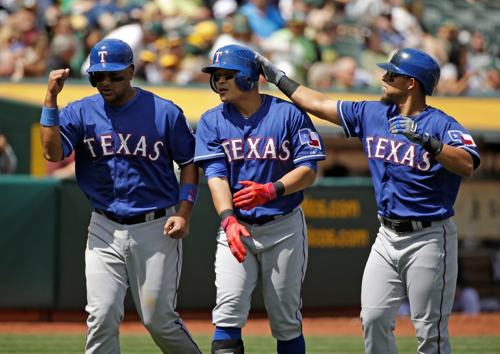 Texas Rangers' Shin-Soo Choo, center, of South Korea, is greeted by teammates Carlos Corporan, left, and Rougned Odor, right, after hitting a three run homer off Oakland Athletics starting pitcher Kendall Graveman in the fourth inning of their baseball game Thursday, April 9, 2015, in Oakland, Calif. (AP Photo/Eric Risberg)