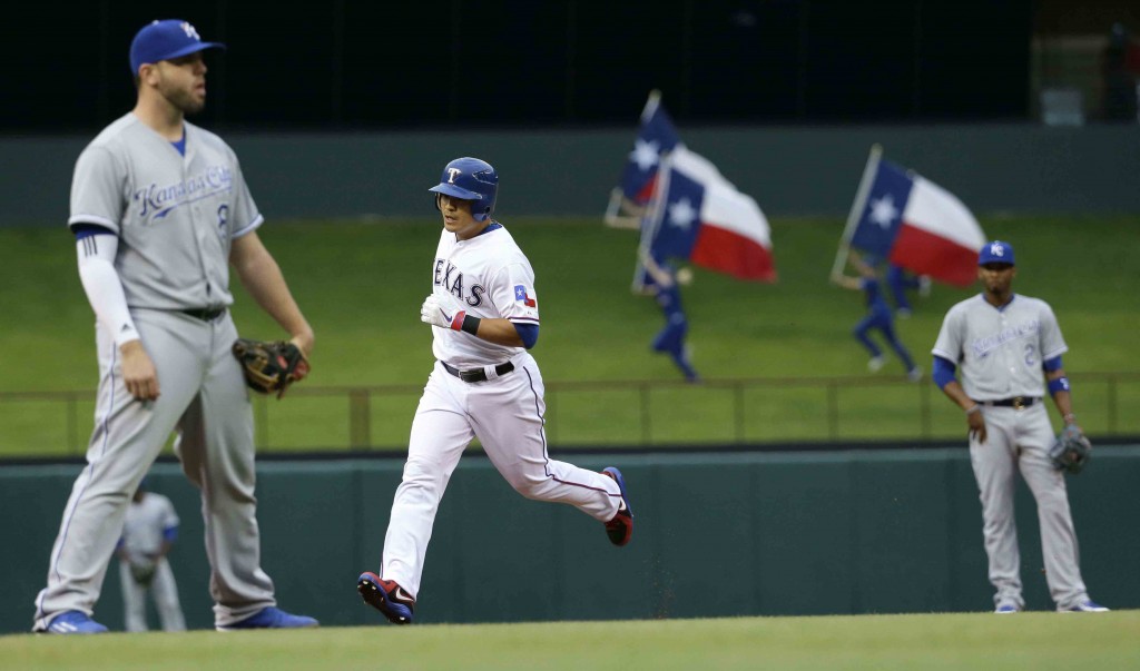 Texas Rangers Shin-Soo Choo, center, rounds the bases after a solo home run as Kansas City Royals shortstop Alcides Escobar (2) and third baseman Mike Moustakas (8) look on during the first inning of a baseball game in Arlington, Texas, Tuesday, May 12, 2015. (AP Photo/LM Otero)